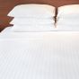 A bed with many pillows and Swiss stripes sheets.